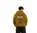 Person wearing a mustard yellow hoodie with car graphics on the back, standing against a white background